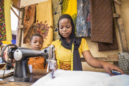 Person using a sewing machine and a child standing behind the person