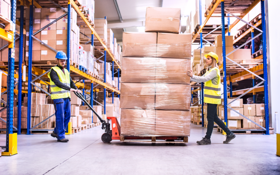 Two persons moving cardboard boxes in a warehouse